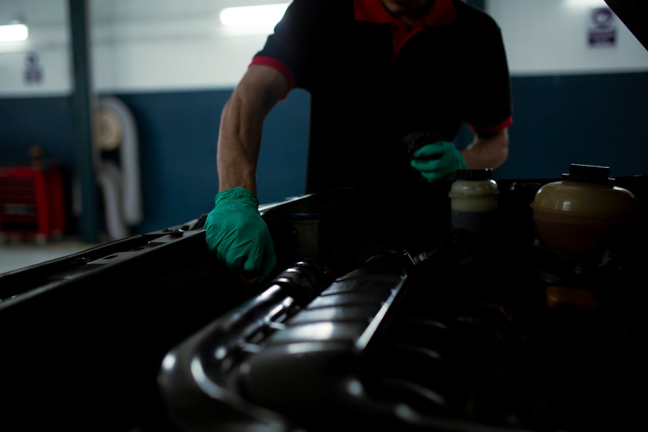 Mechanic in gloves inspecting car engine in a well-lit garage setting.